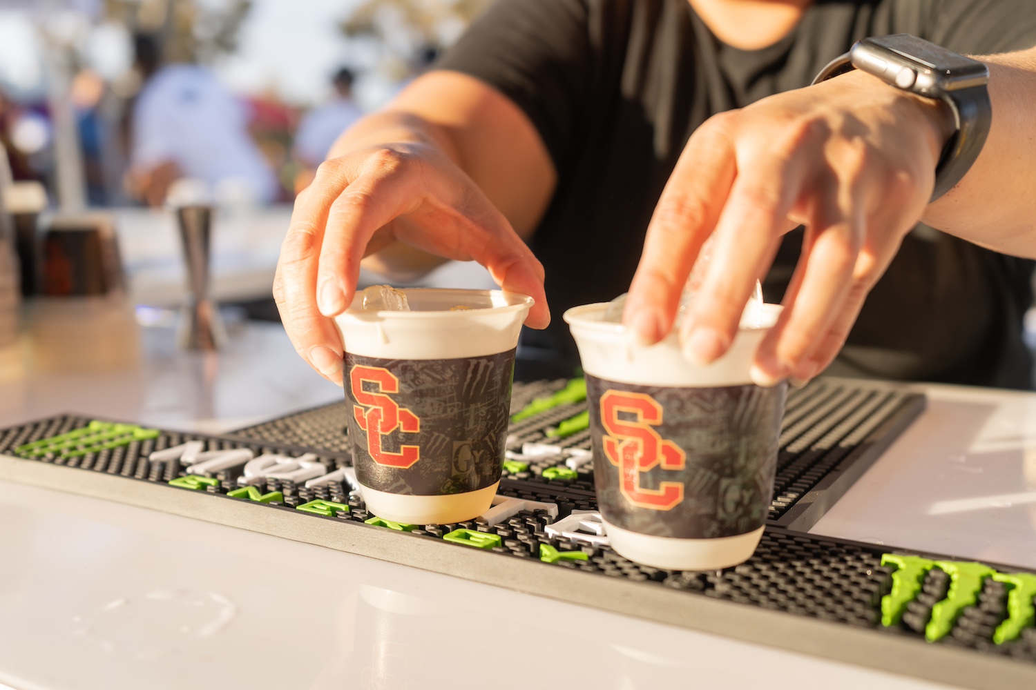 A bartender at a football game makes drinks in Better for All cups with the University of Southern California logo on them.